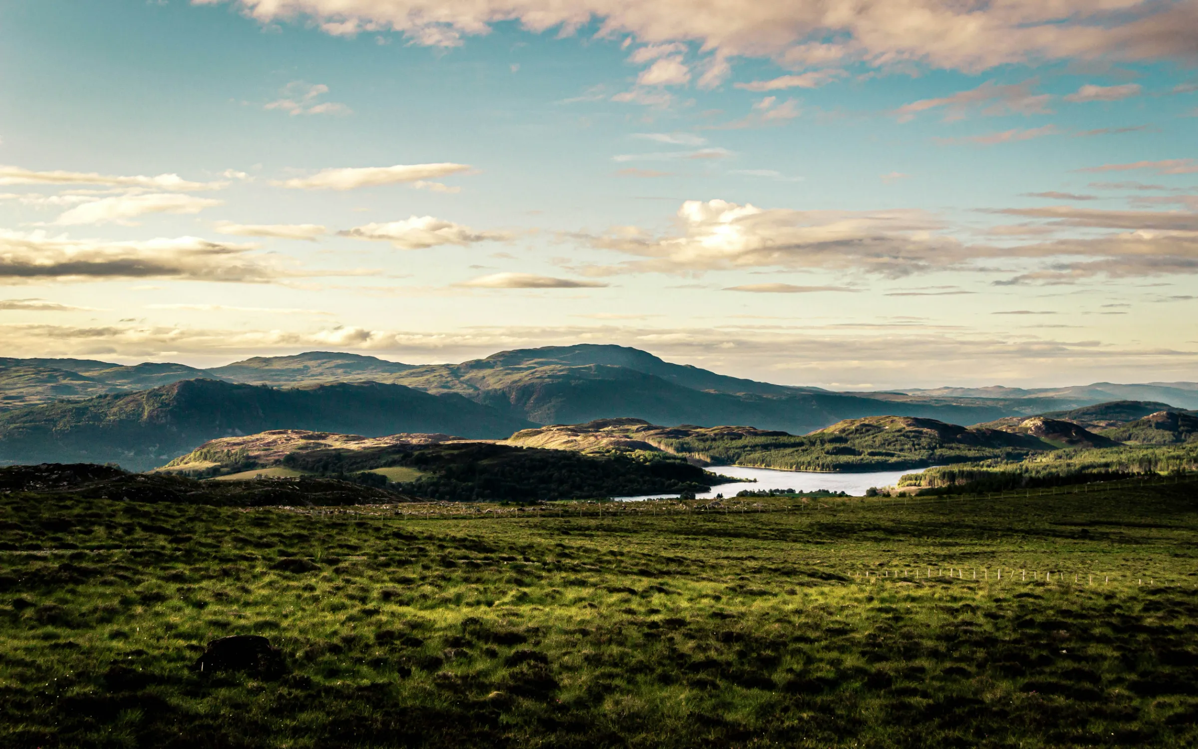 Green highland hills running down to a loch under an evening sky